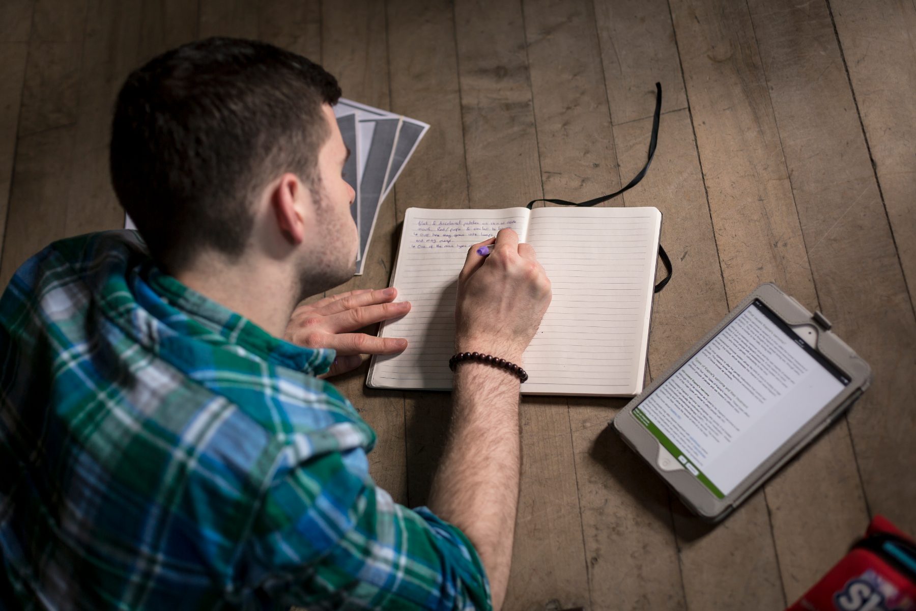 An actor lying on the studio floor, writing in a notebook beside a tablet